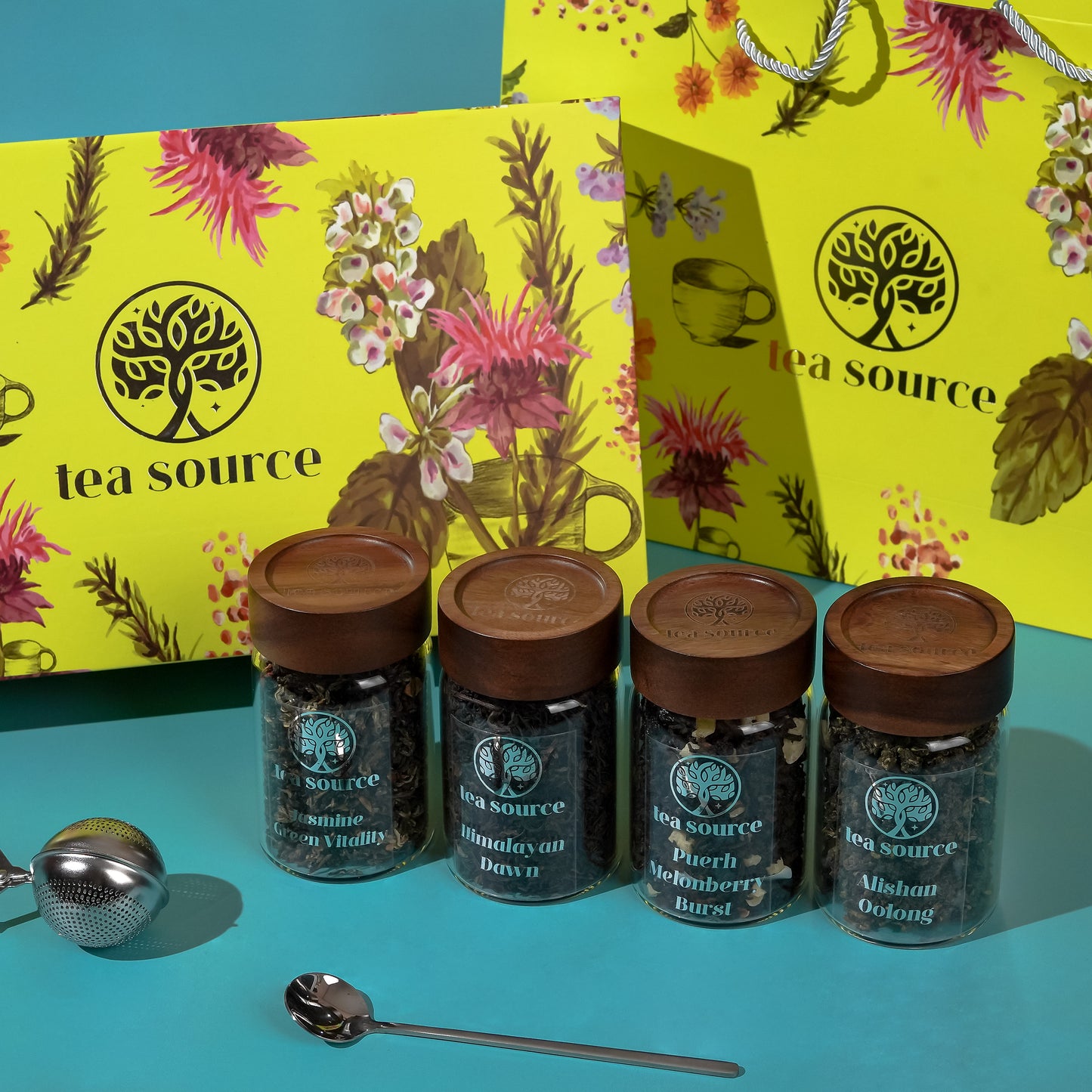 Tea Source Energy Vitalitea Infusion Set – four glass jars of premium loose leaf teas (Jasmine Green Tea, Himalayan Dawn, Puerh Melonberry Burst, and Alishan Oolong) with wooden lids, displayed alongside a yellow floral gift box, matching paper bag, tea infuser, and spoon.