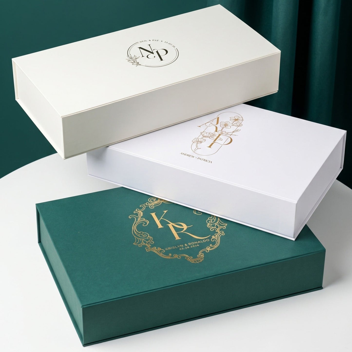 Three custom tea gift boxes with personalized monogram foil designs in cream, white, and green