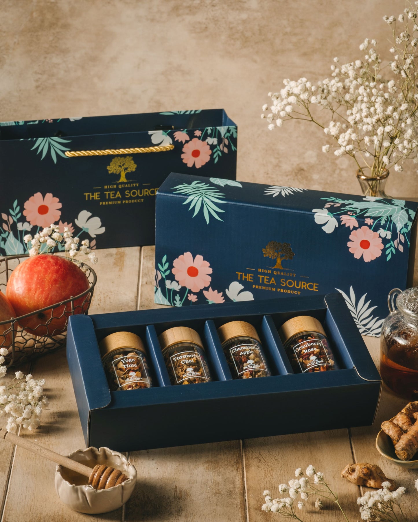 Tea Source gift set with four glass jars of assorted teas in a floral blue box, displayed with a matching paper bag and tea accessories.